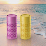 Load image into Gallery viewer, Nöz purple and yellow tinted sunscreen sitting on beach
